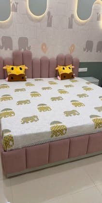 Upholstered pink bed below an elephant-motif wall with backlit panels