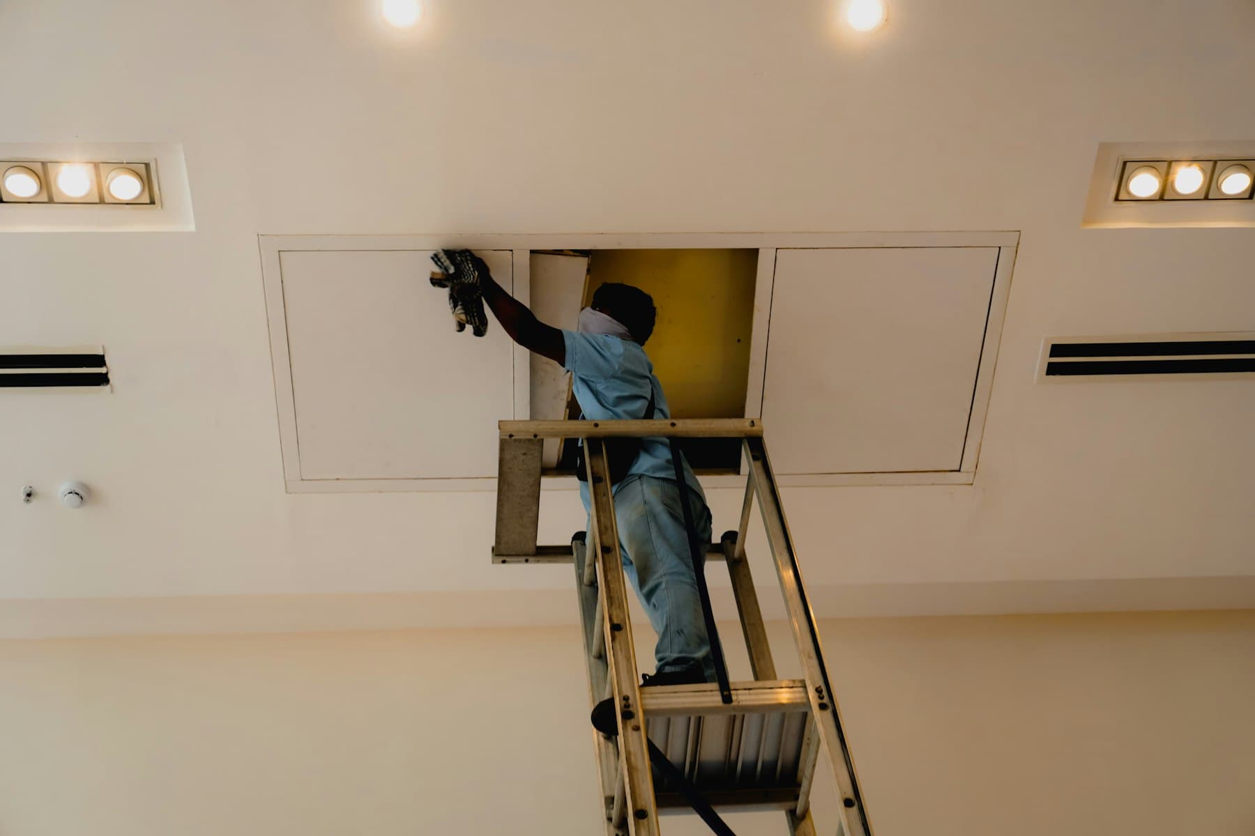 Technician working through a ceiling access panel in a finished room
