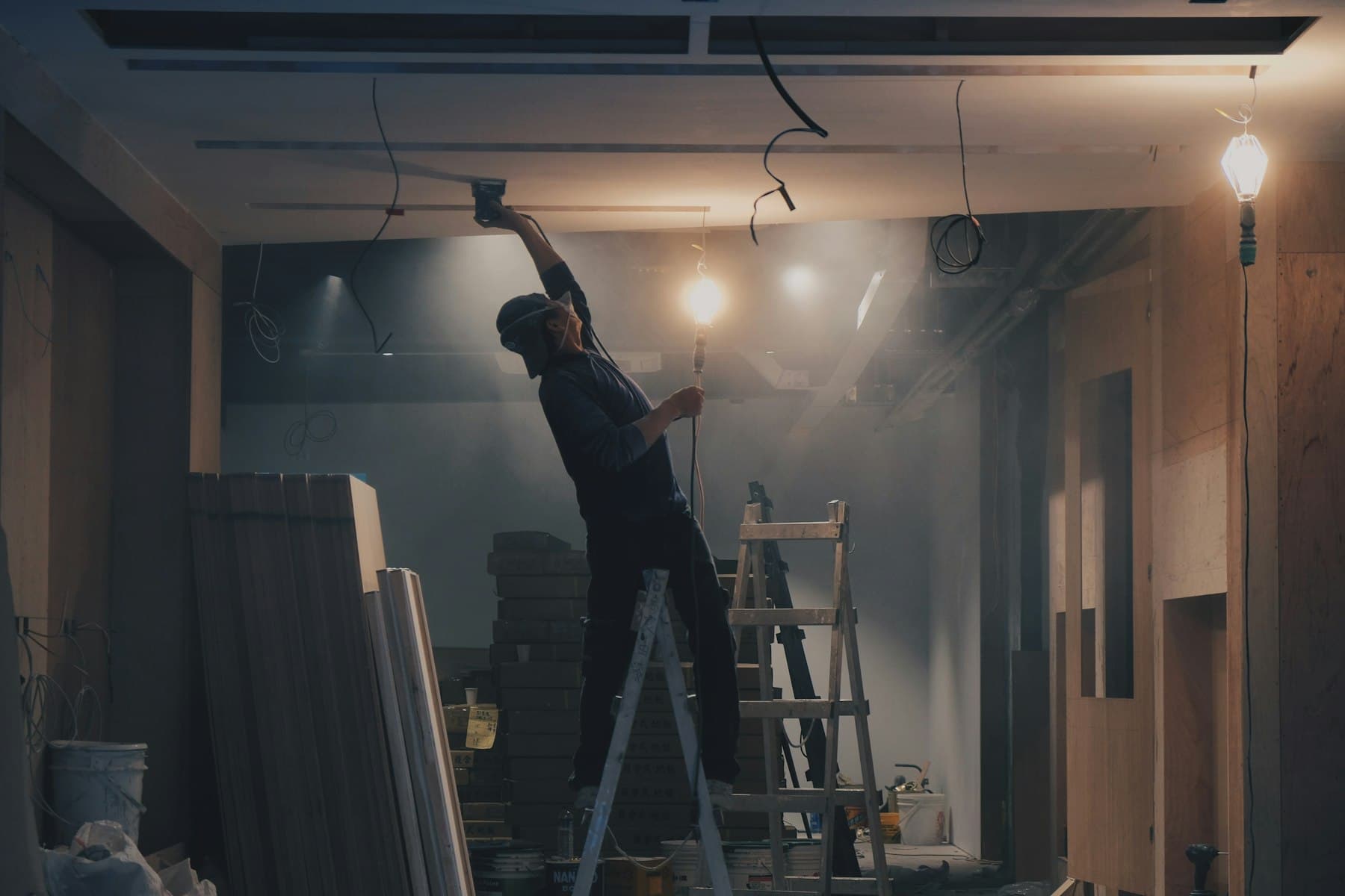 Tradesman on a ladder fitting ceiling works in a warmly lit interior