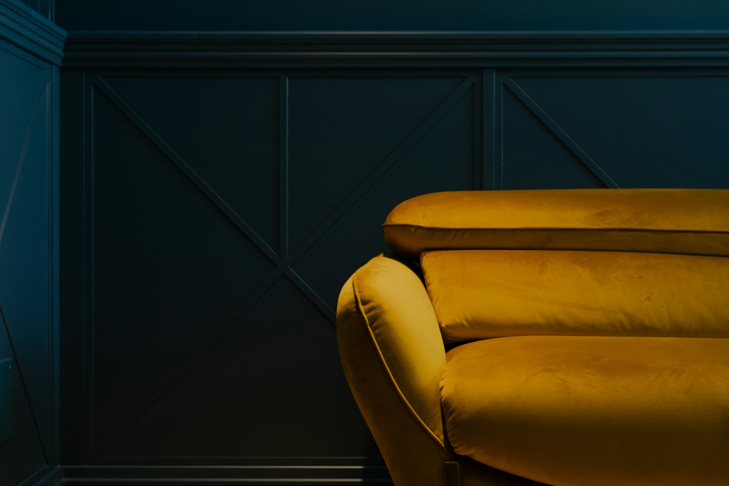 Mustard velvet sofa against a deep blue panelled wall